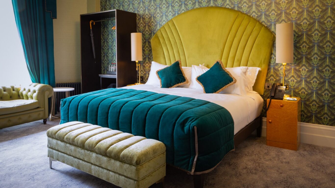 Luxurious hotel room with plush teal bed, elegant armchair, and stylish decor, offering a relaxing and welcoming retreat.