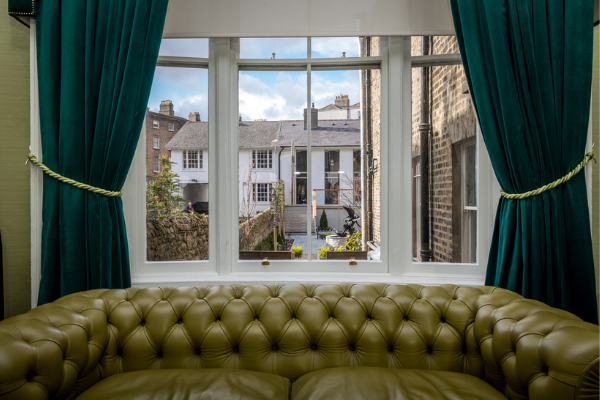 Cosy lounge with plush leather sofa, large window view of charming brick buildings, and elegant teal curtains.