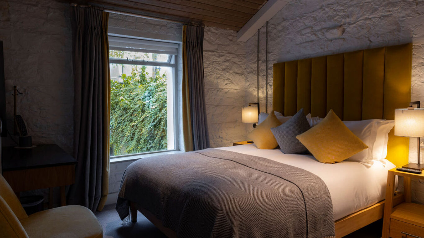 Cosy hotel room with plush yellow decor, comfy bed, soft lighting, and garden view, promising a relaxing stay.