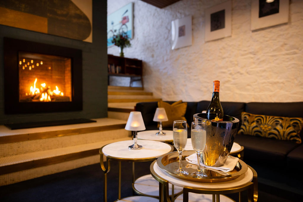 Cosy hotel lounge with a crackling fireplace, plush sofas, and a champagne setup for a relaxing retreat experience.