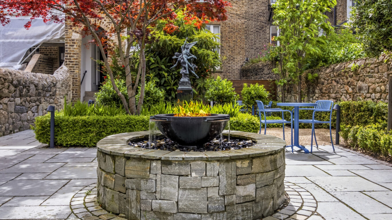 Charming hotel courtyard with a tranquil stone fountain, lush greenery, and inviting seating, perfect for relaxation.