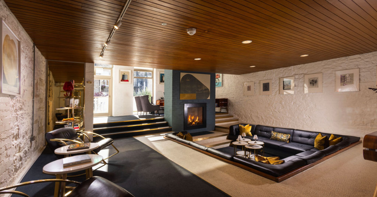 Cosy hotel lounge with fireplace, stylish sunken seating area, chic decor, and art-adorned walls. Ideal for relaxation.