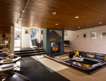 Cosy hotel lounge with fireplace, stylish sunken seating area, chic decor, and art-adorned walls. Ideal for relaxation.
