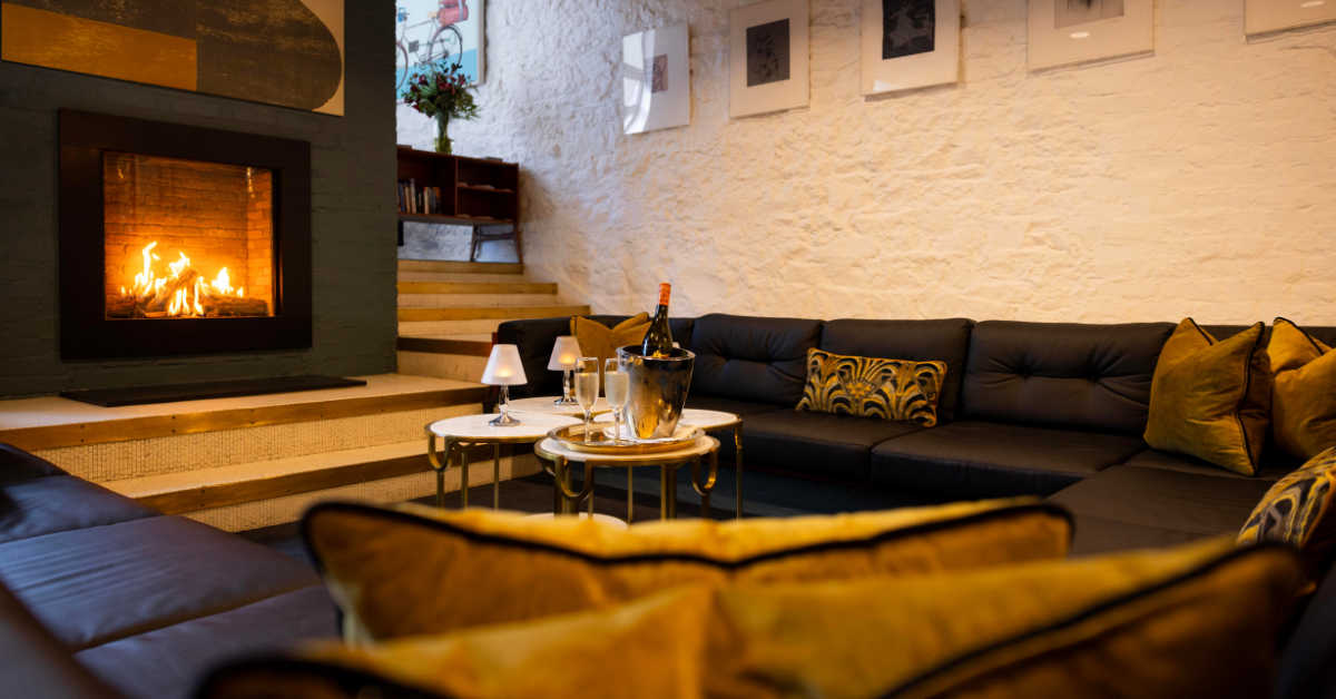 Guests relax by a cosy fire in a stylish lounge with plush sofas, soft lighting, and elegant decor, ideal for leisure stays.